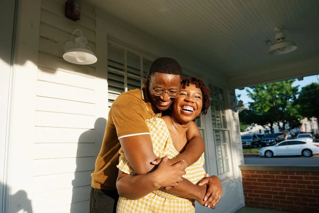 A man and a woman embracing and laughing together on a sunlit porch