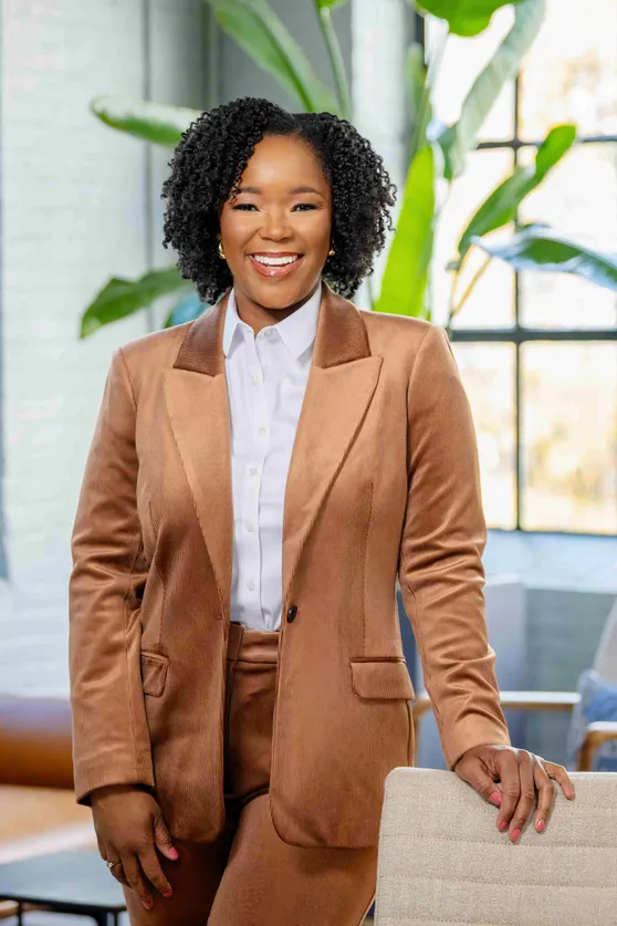 Dr. Simone Gillon-Wright in a tan corduroy suit, standing beside a cream armchair