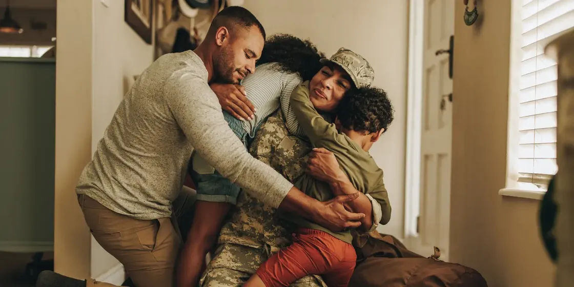 A service member in uniform held in a family embrace as she is welcomed home